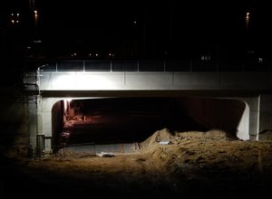 Neubau der westlichen Eisenbahnbrücke mit darunterliegender Tunneldecke im Dunkeln, von Bauscheinwerfern erleuchtet.