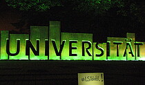 Schriftzug Universität in Magdeburg, nachts grün angestrahlt.
