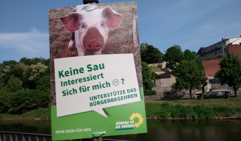 Plakat zum Bürgerbegehren gegen den Schlachthof in Bernburg vor der Silouhette Bernburgs.
