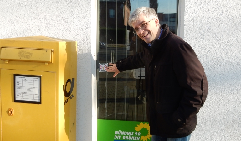 Olaf Meister zeigt am Fenster des Wahlkreisbüros auf das Logo des Freifunk-Aufklebers.