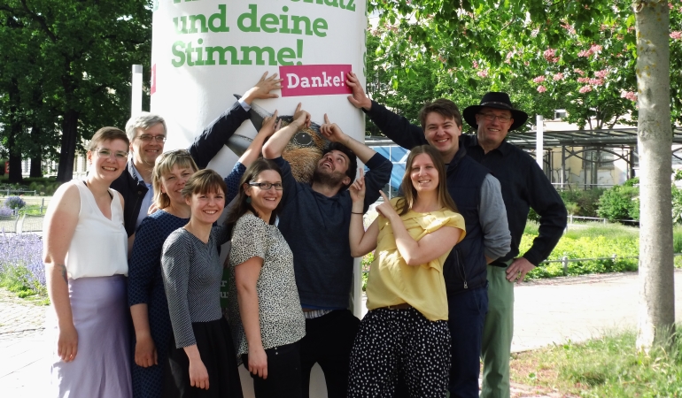 Grüne Stadtratskandidat*innen vor einer Litfaßsäule mit Europawahlmotiv und Störer "Danke".