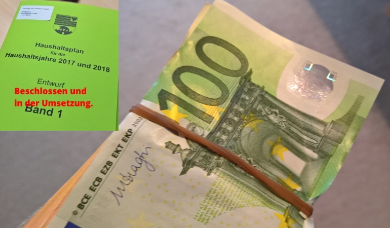 Euro-Geldbündel mit Titelbild des Landeshaushaltes im Hintergrund. Euro-Geldbündel mit Titelbild des Landeshaushaltes im Hintergrund.