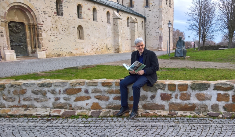Olaf Meister sitzt mit einem Buch auf einer niedrigen Mauer vom dem Kloster Unserer Lieben Frauen.