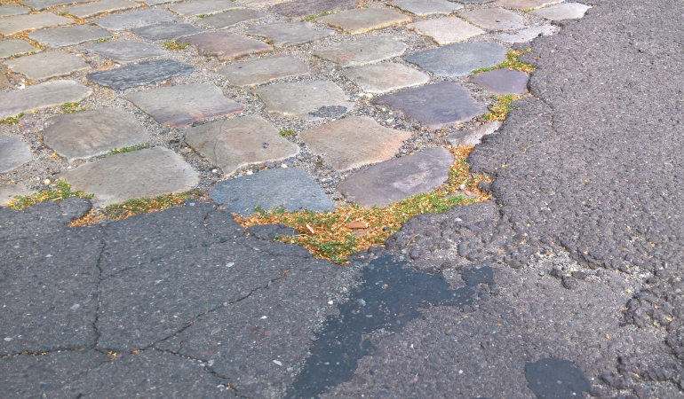 Reparaturbedürftige Straße mit Asphalt und Kopfsteinpflaster. Reparaturbedürftige Straße mit Asphalt und Kopfsteinpflaster.