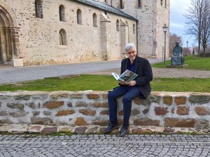 Olaf Meister sitzt mit einem Buch auf einer niedrigen Mauer vom dem Kloster Unserer Lieben Frauen.