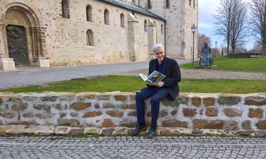 Olaf Meister sitzt mit einem Buch auf einer niedrigen Mauer vom dem Kloster Unserer Lieben Frauen.