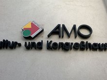 Logo des AMO an der Hauswand.