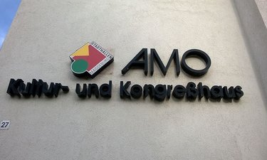 Logo des AMO an der Hauswand.