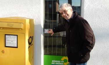 Olaf Meister zeigt am Fenster des Wahlkreisbüros auf das Logo des Freifunk-Aufklebers.