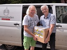 Olaf Meister (rechts) übergibt 2 Klassensätze Terminplaner des Landtages in einem Karton an Ingo Block vom Umsonstladen Salbke e. V. Im Hintergrund der Transporter des Vereins.