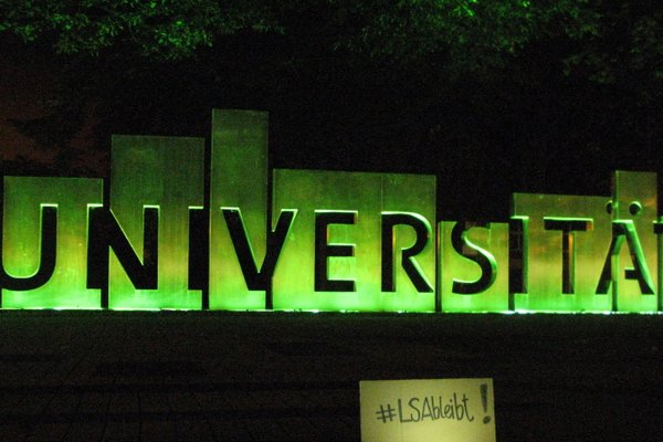 Eingang OVGU mit dem plastischen Schriftzug "Universität" grün beleuchtet.