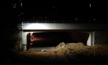 Neubau der westlichen Eisenbahnbrücke mit darunterliegender Tunneldecke im Dunkeln, von Bauscheinwerfern erleuchtet.