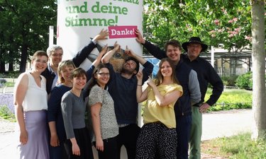 Grüne Stadtratskandidat*innen vor einer Litfaßsäule mit Europawahlmotiv und Störer "Danke".