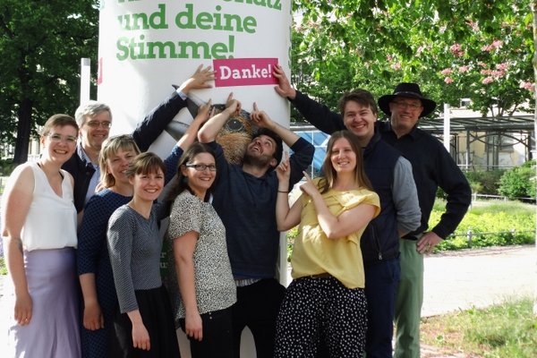 Grüne Stadtratskandidat*innen vor einer Litfaßsäule mit Europawahlmotiv und Störer "Danke".