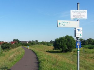 Blick auf den Elberadweg in Pechau entlang des asphaltierten Weges auf des Deichkrone. Vorn ein Hinweisschild auf den Elberadweg und den Pechauer Platz.